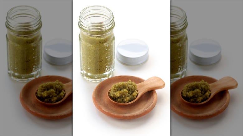 Yuzu kosho in a glass jar and on a wooden spoon against a white background