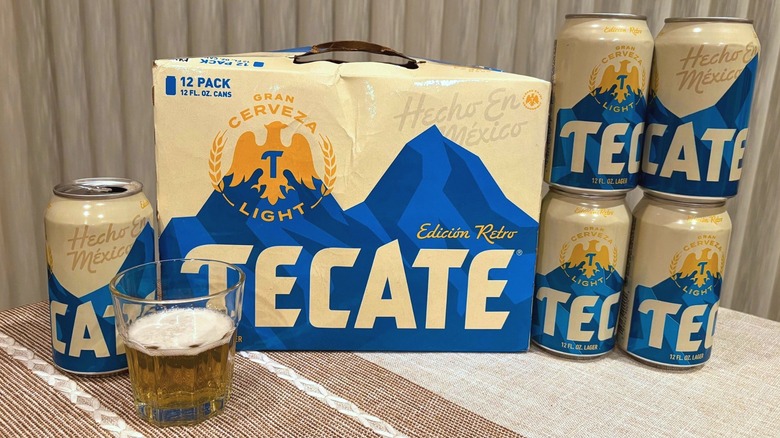 A package of Tecate surrounded by cans and a glass