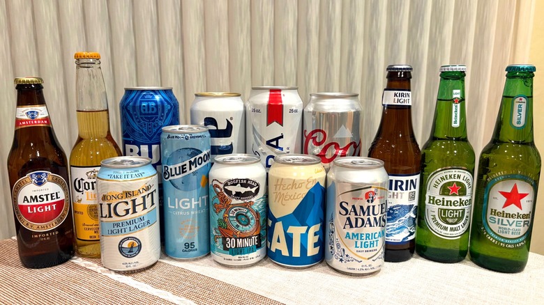 A group of light beers all lined up against a cream curtain/yellow wall