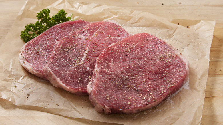 Lean beef steaks on parchment paper.