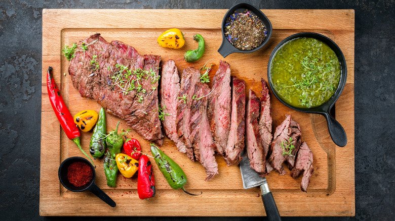 A London broil steak on a cutting board with sauces and sides