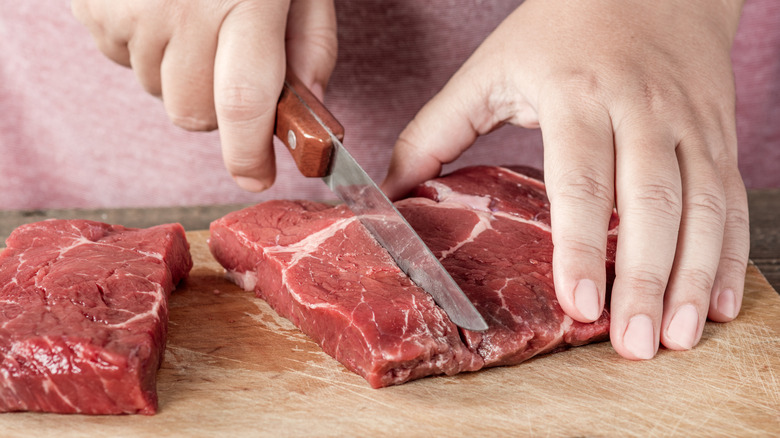 A person scoring a raw steak on a cutting board
