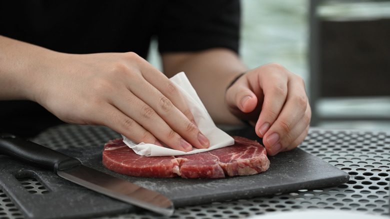 A person patting a steak dry with paper towel