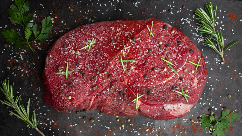 A raw steak seasoned with salt, pepper, and rosemary