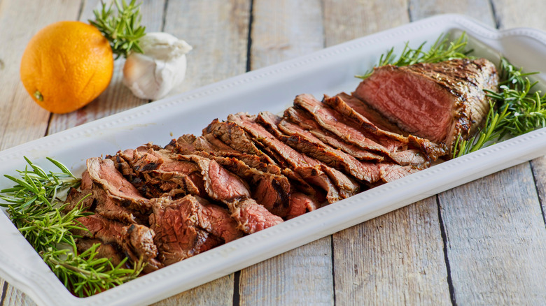 A sliced London Broil on a plate with rosemary