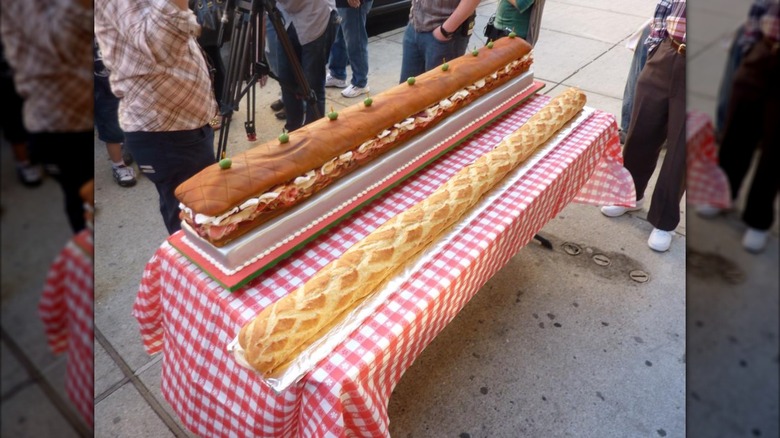 A hero cake and hero sandwich next to each other on a red checkered tablecloth
