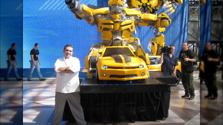 The Cake Boss standing next to a Camaro and Bumblebee Transformers cake