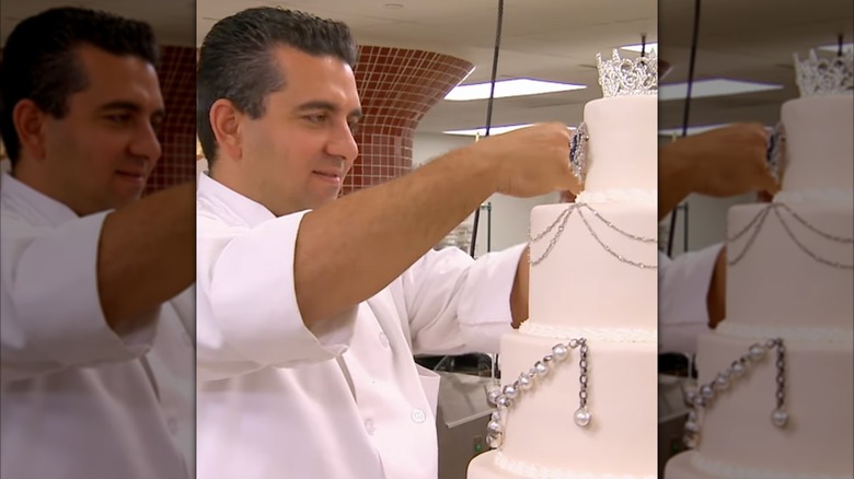 The Cake Boss adding jewels to a tiered white cake