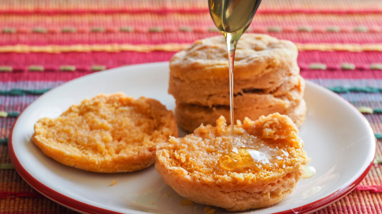 A spoon drizzling honey on a sweet potato biscuit