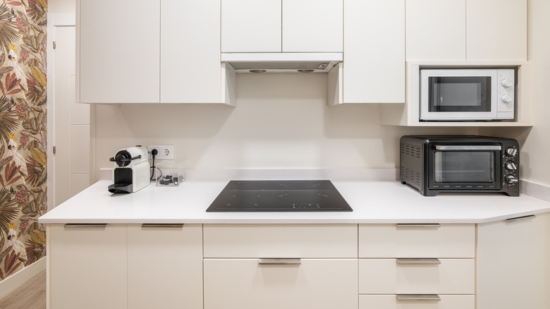A kitchen with white cabinets, a microwave in a cubby over a toaster oven, and a glass range