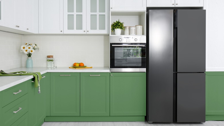 Kitchen with white upper cabinets and countertops, green base cabinets, and a black refrigerator