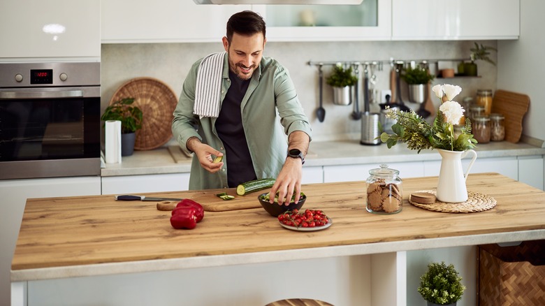 Man smiling and preparing salad on large kitchen island