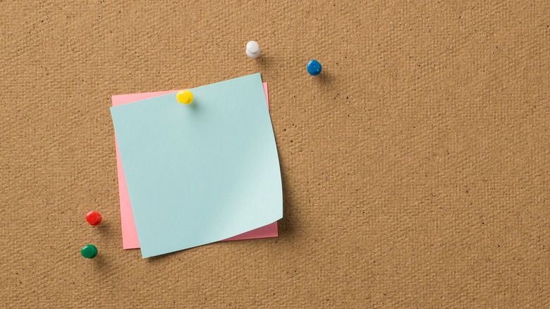 Cork board with multicolor pushpins and pink and blue squares of paper
