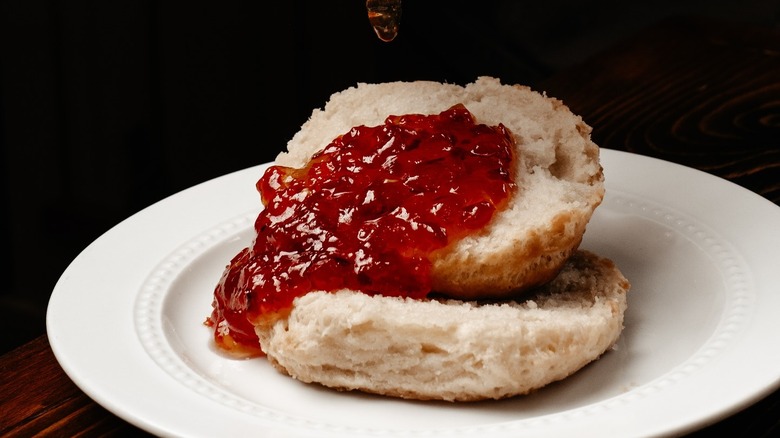 Two halves of a buttermilk biscuit covered in red jam
