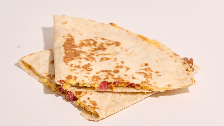 bacon quesadilla cut in half on a white table