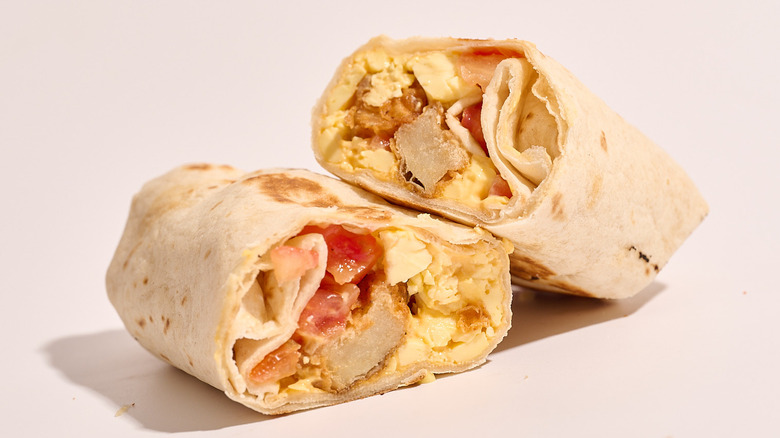burrito filled with potato, cheese, and tomato sliced in half on a table