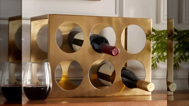 Metal wine rack on wood countertop next to plant and glass of wine.