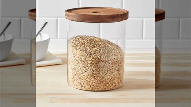 Glass jar with wood lid containing dry goods on countertop.