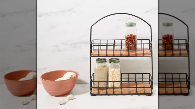 Two-tiered spice rack made of metal and wood on countertop next to bowl.