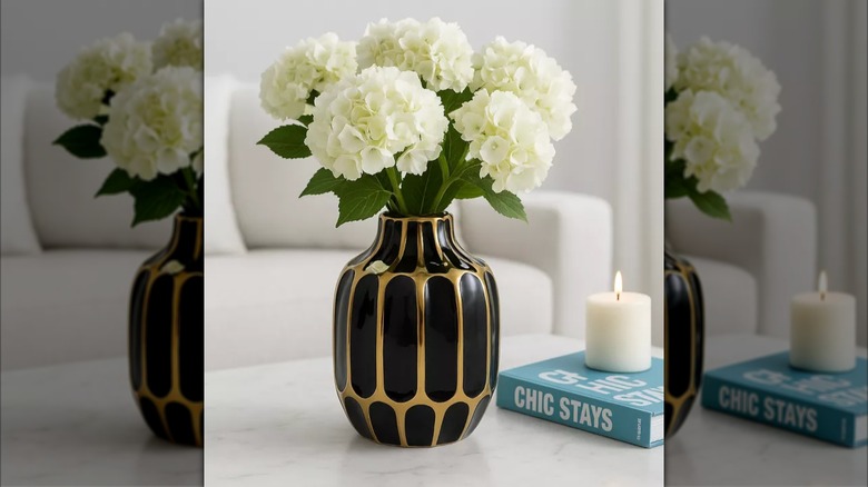 Black and gold sculptural flower vase with white flowers next to book and candle.