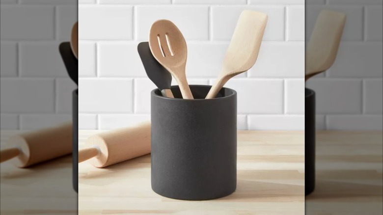 Stoneware utensil holder with various kitchen utensils inside on wood countertop.