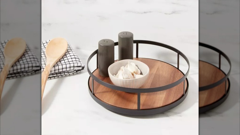 Wood and metal lazy susan holding spices and bowl of garlic on marble counter.