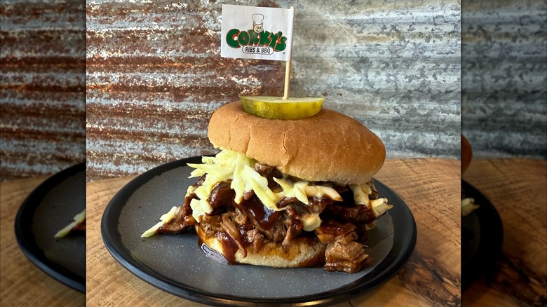 A barbecue brisket sandwich with slaw and a pickle speared with a Corky's toothpick