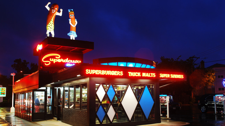 The exterior of Superdawgs with an illuminated sign and hot dog statues on the roof
