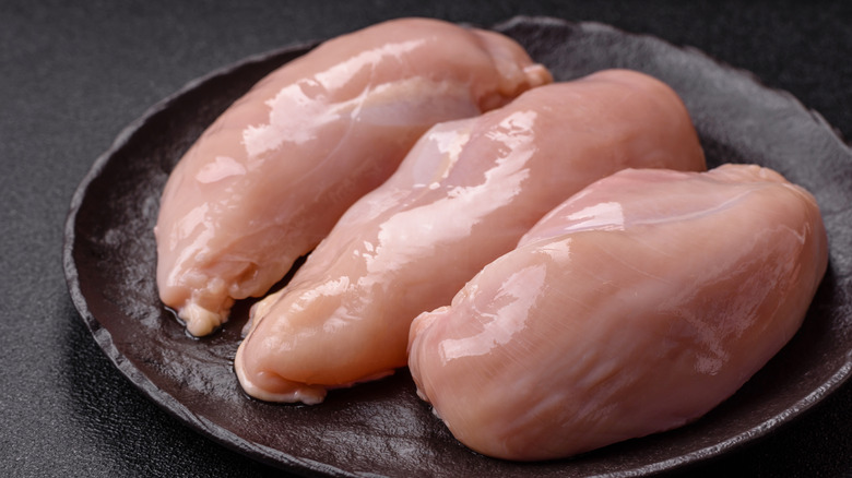 Three raw chicken breasts on a black plate against a dark background