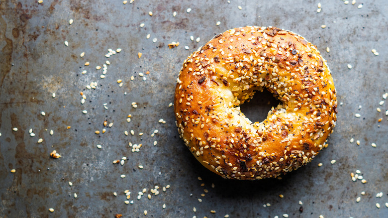 an everything bagel on grey background with its seasonings spread everywhere