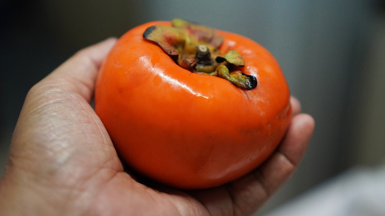 a person's hand holding a persimmon
