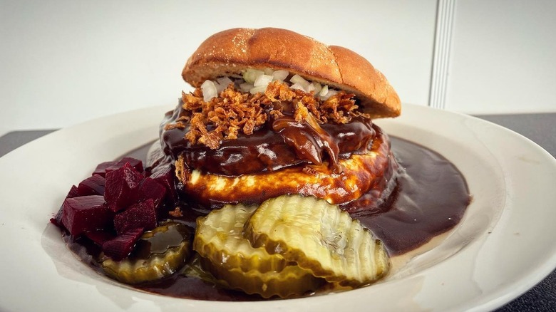 A bøfsandwich on a plate with pickles and beets