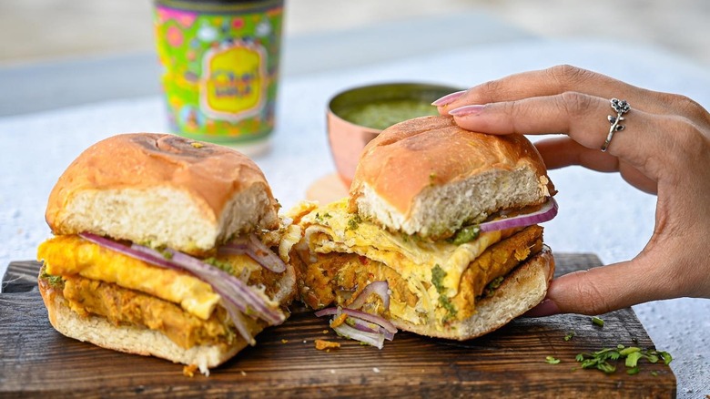 A person taking a bun kebab from a wooden serving board
