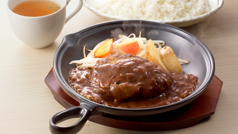A japanese hambagu on a plate with gravy and vegetables