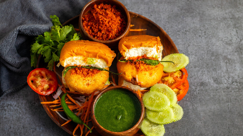 Two vada pav burgers on a plate with condiments and garnishes