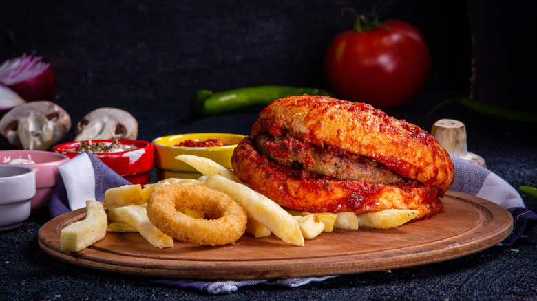 An islak burger on a wooden cutting board with fries and onion rings