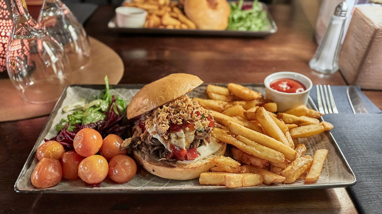 A pulled reindeer burger on a tray with fries, salad, and tomatoes