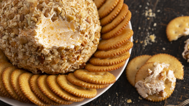 A cheeseball with nuts on a plate with crackers