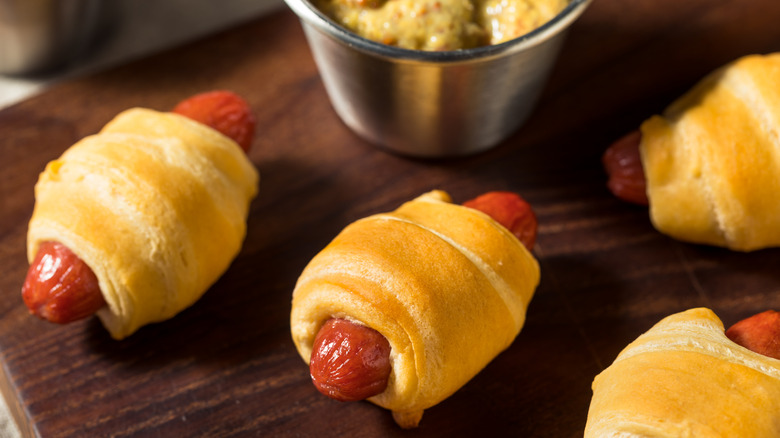 Pigs in a blanket on a wooden cutting board with mustard