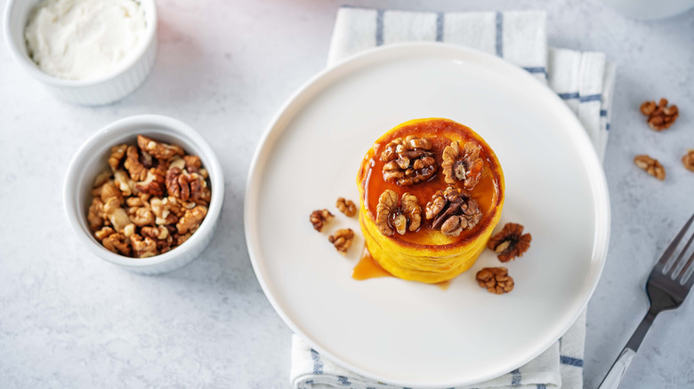 a stack of sweet potato pancakes topped with walnuts and syrup
