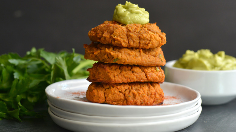 a pile of sweet potato lentil falafel patties with a green sauce on top