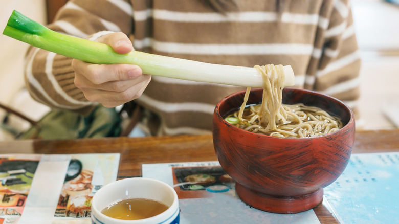 person dipping leek in noodles with sauce nearby