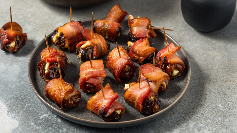 Bacon-wrapped dates stuffed with cheese served on a dark plate