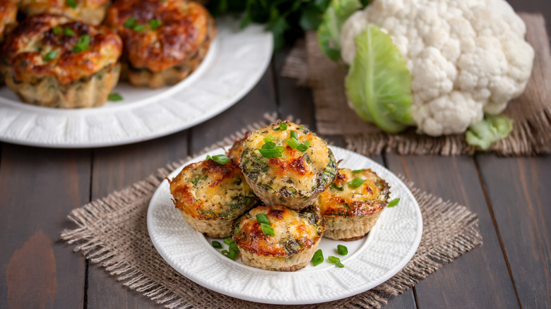 Cauliflower egg bites on a plate with a head of raw cauliflower in the background