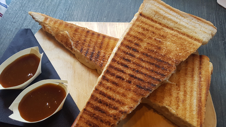 A halved grilled cheese sandwich is next to barbecue sauce