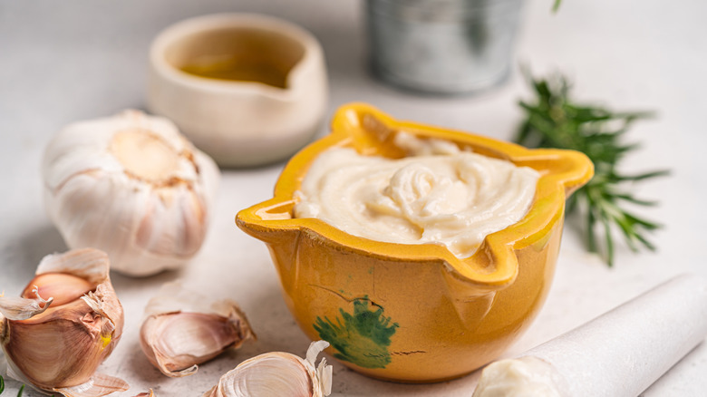 Garlic aioli sits in a mortar and surrounded by its ingredients
