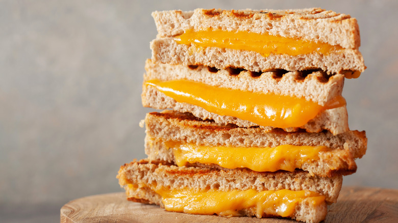 Two halved grilled cheese sandwiches sit stacked on a round wood cutting board
