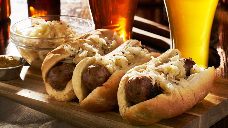 Three German bratwurst sausages with sauerkraut on a wooden board