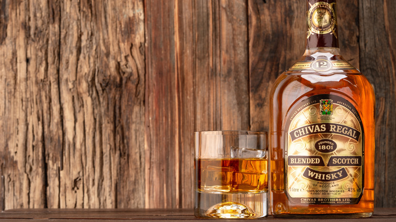 A bottle and glass of Chivas Regal 12 Year with a wooden background