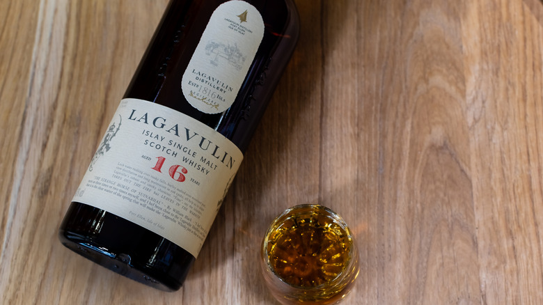 A bottle of Lagavulin 16 Year lying on a table with a neat pour in a glass